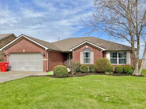 A two-story brick house with a garage, a front yard with a lawn, and a tree.