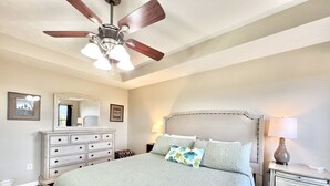 Ein Schlafzimmer mit Bett, Schminktisch, Nachttisch, Deckenventilator und Spiegel.
