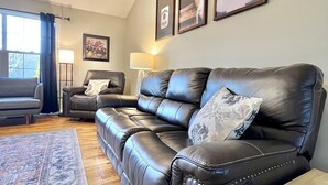 Ein Wohnzimmer mit einem schwarzen Ledersofa, einem gemusterten Teppich und gerahmten Bildern an der Wand.