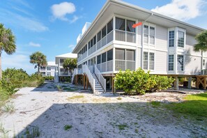 A coastal building with multiple balconies, a staircase leading to the upper levels, and a sandy beach area.