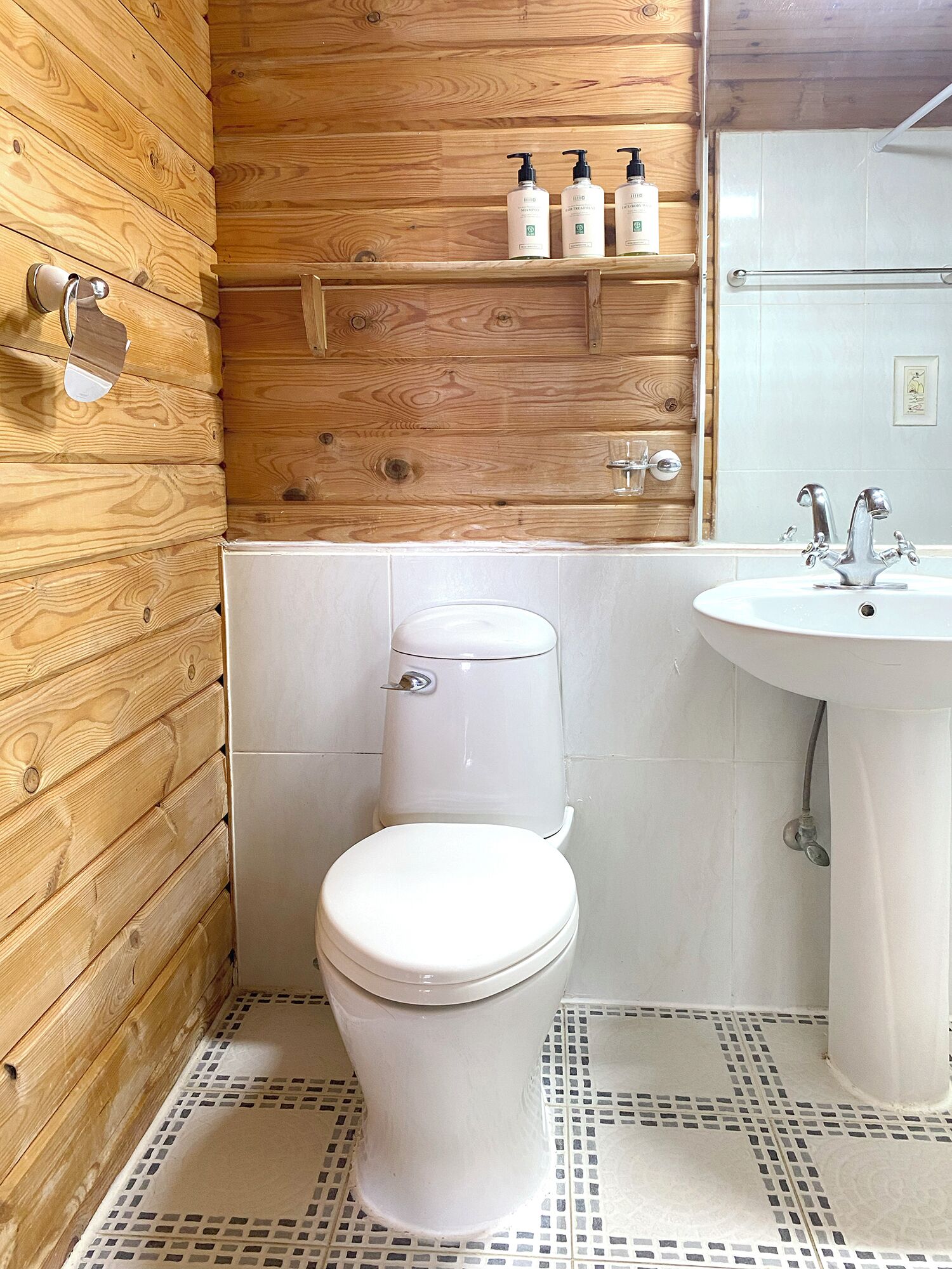 Un baño con inodoro blanco, lavamanos y paneles de madera en las paredes.
