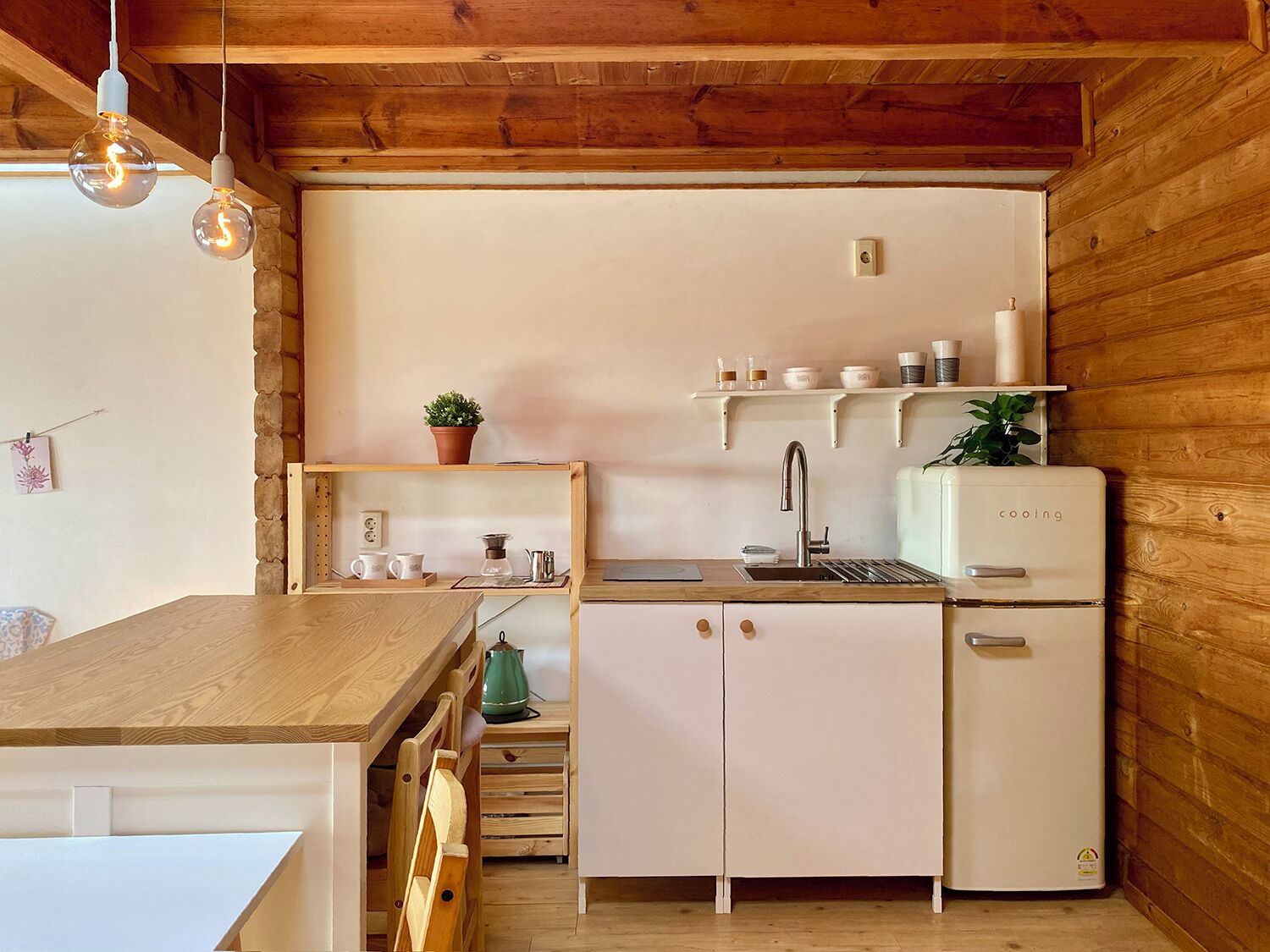 A compact kitchen with wooden beams, a white refrigerator, a sink, and a wooden table.