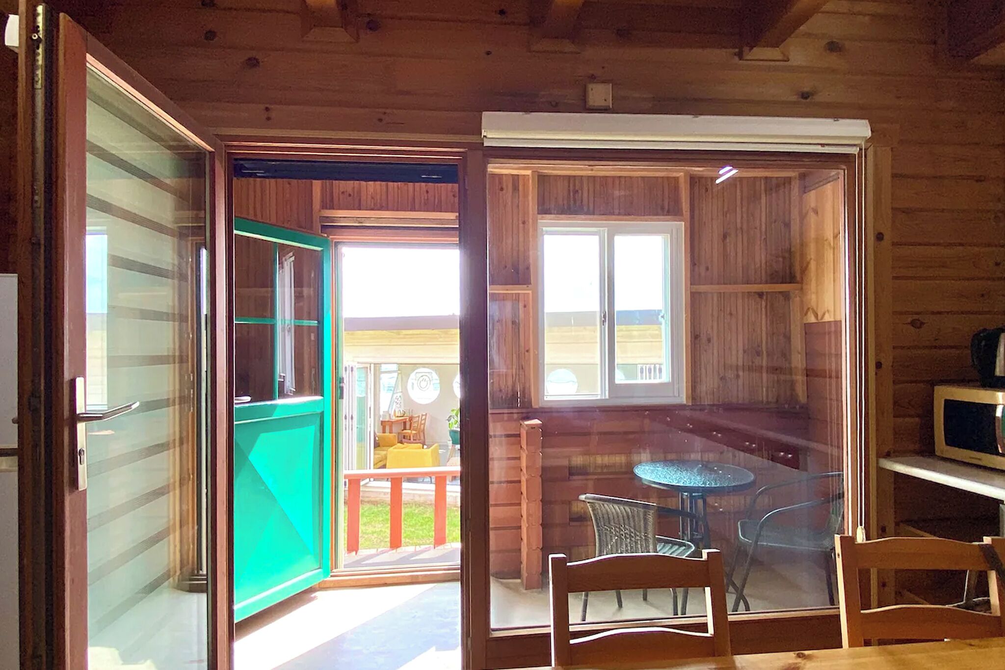 Una cabaña de madera con un ventanal de vidrio que da a un balcón con una mesa y sillas.