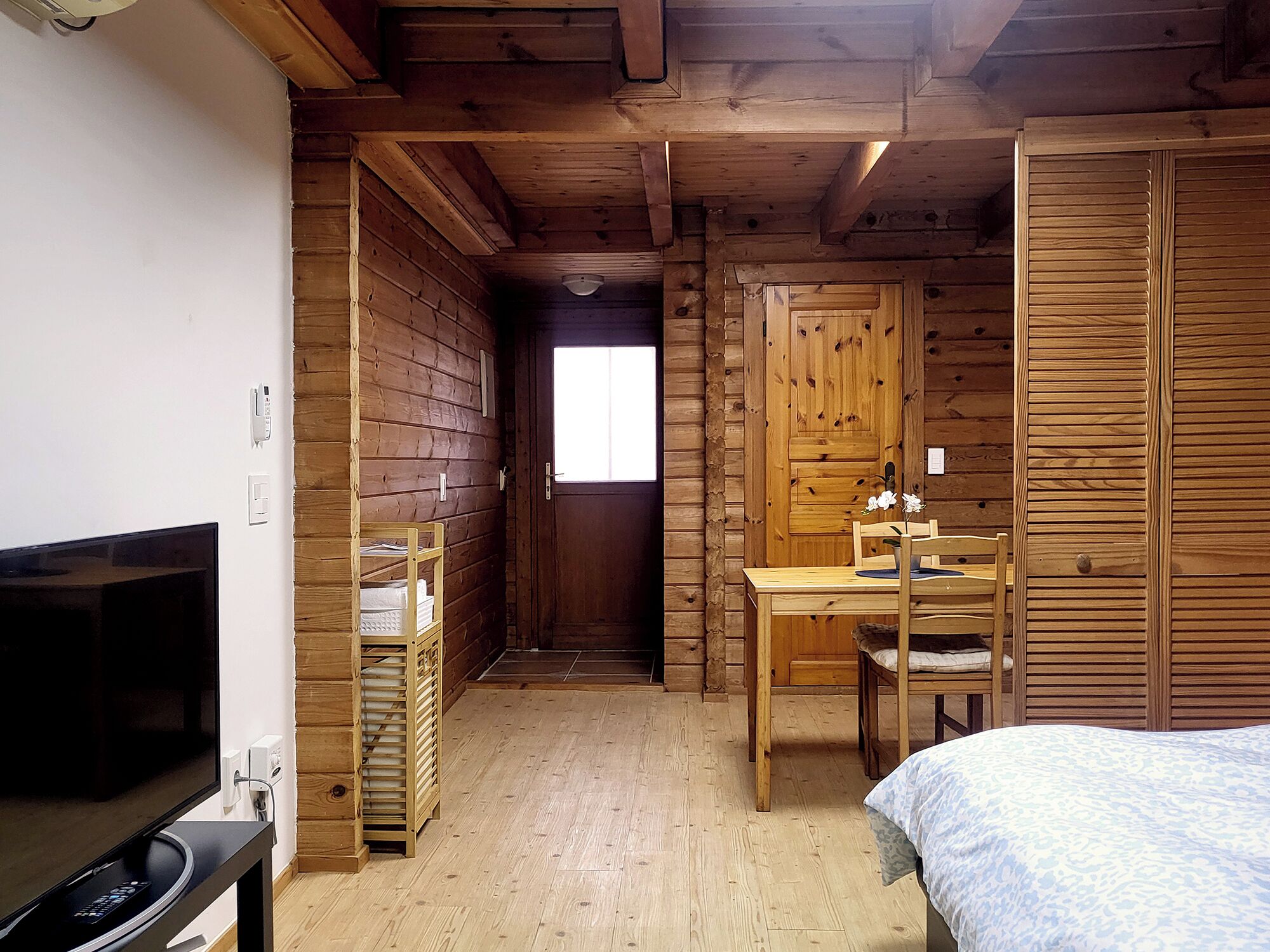 A wooden cabin room with a bed, a desk, a chair, a television, and a window.