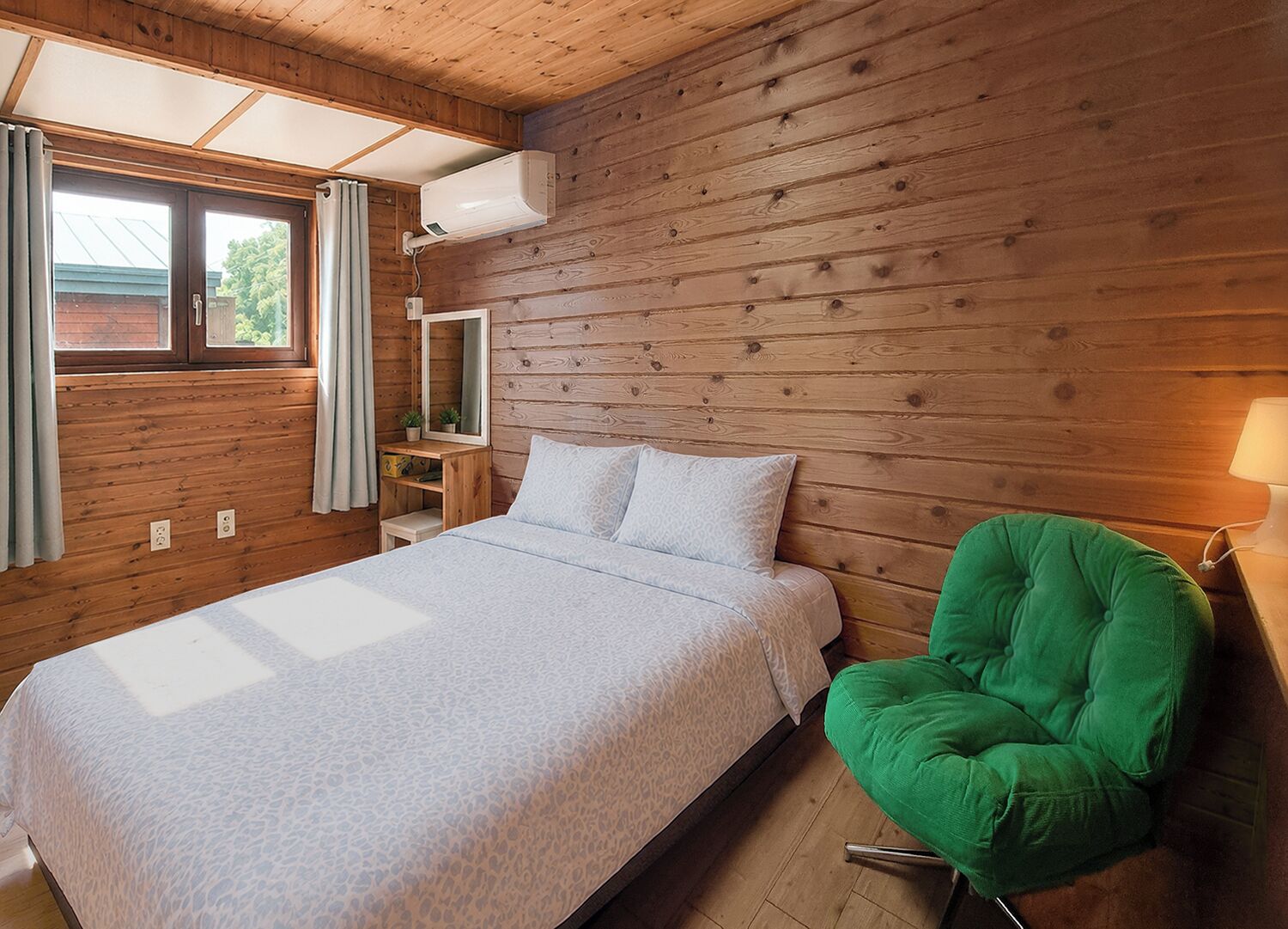 A bedroom with a bed, a green chair, a nightstand, a mirror, and a window with curtains.