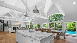 A spacious living area with a large marble island, a dining area with a pool view, and a modern kitchen with white cabinetry. - Bay Breeze Escape—Pool, Game Room & Views (Centerville)