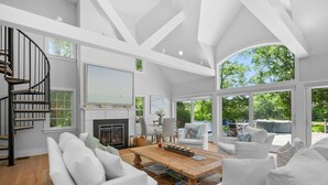 A spacious living room with a fireplace, white sofas, a wooden coffee table, and a spiral staircase. - Bay Breeze Escape—Pool, Game Room & Views (Centerville)