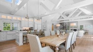 A spacious kitchen with white cabinetry, a wooden dining table, and a large island. - Bay Breeze Escape—Pool, Game Room & Views (Centerville)