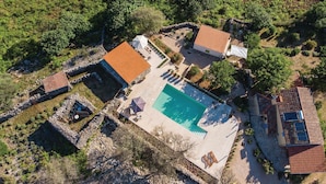 Vista aérea de una propiedad con piscina, mobiliario exterior y un muro de piedra.