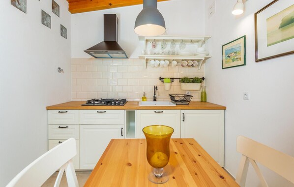 Une cuisine avec des meubles blancs, un plan de travail en bois, une cuisinière à gaz, un évier et un porte-ustensiles suspendu.