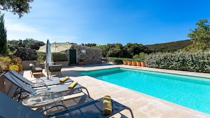 Zona junto a la piscina con sillones de descanso, una mesa con bebidas y un muro de piedra.