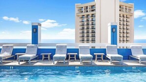 A rooftop pool with lounge chairs and a high-rise building in the background. - Beachside escape w/ ocean view, 22nd floor (Honolulu)