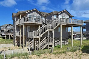 A multi-story beach house with a balcony and a staircase leading to the upper floor.