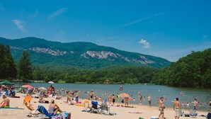 Uma praia com pessoas tomando sol e nadando, rodeada por montanhas e árvores.