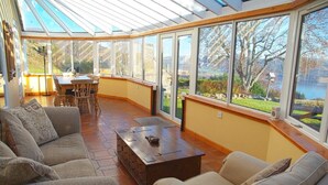 Une véranda avec un toit en verre, une table basse en bois et un coin repas avec des chaises et une table.