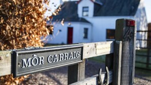 Une pancarte en bois portant l’inscription « MOR CARRAIG » est fixée à une clôture.