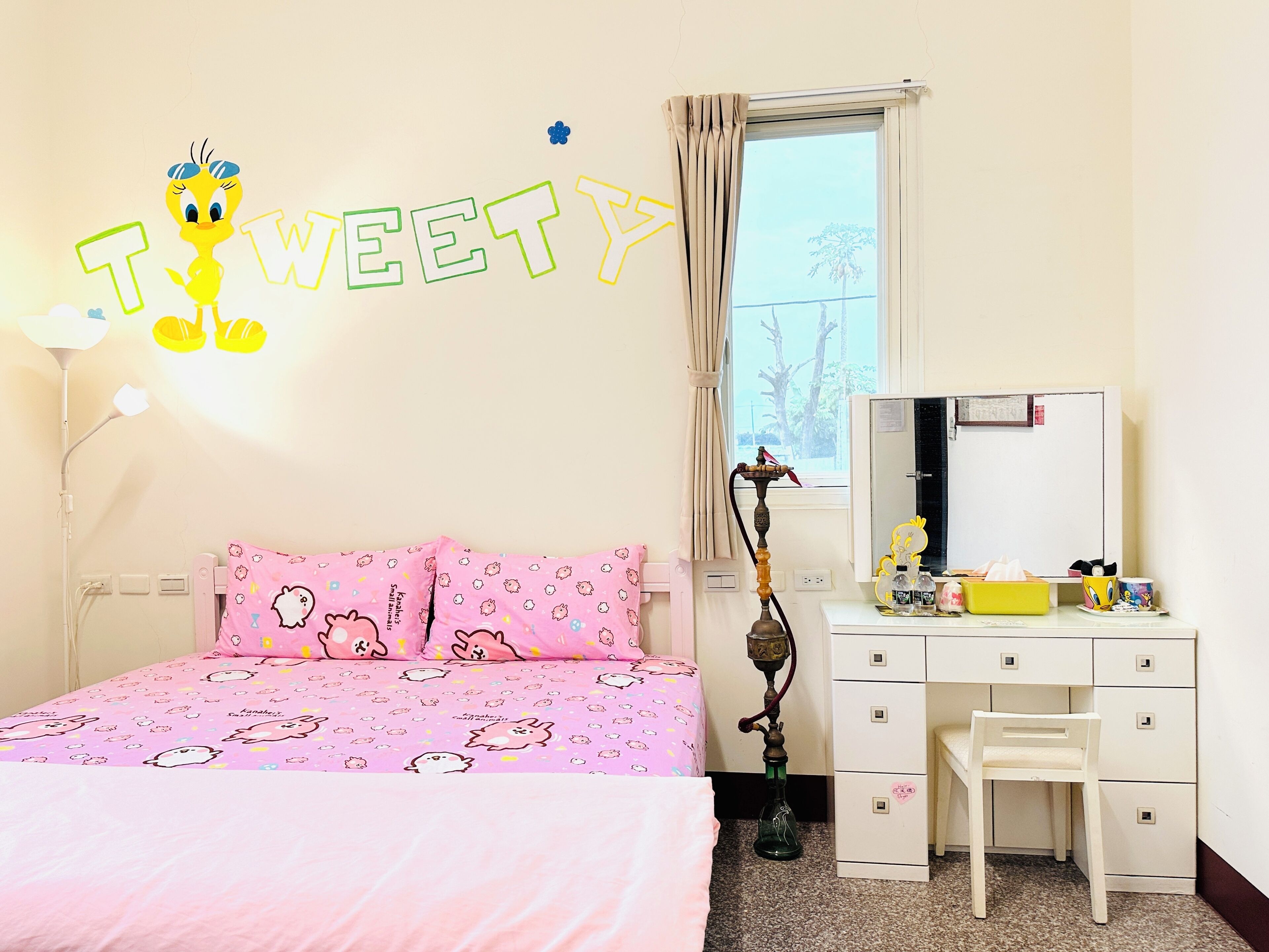 Une chambre à coucher avec une couvre-lit rose, un bureau avec un miroir, une chaise et un narguilé.