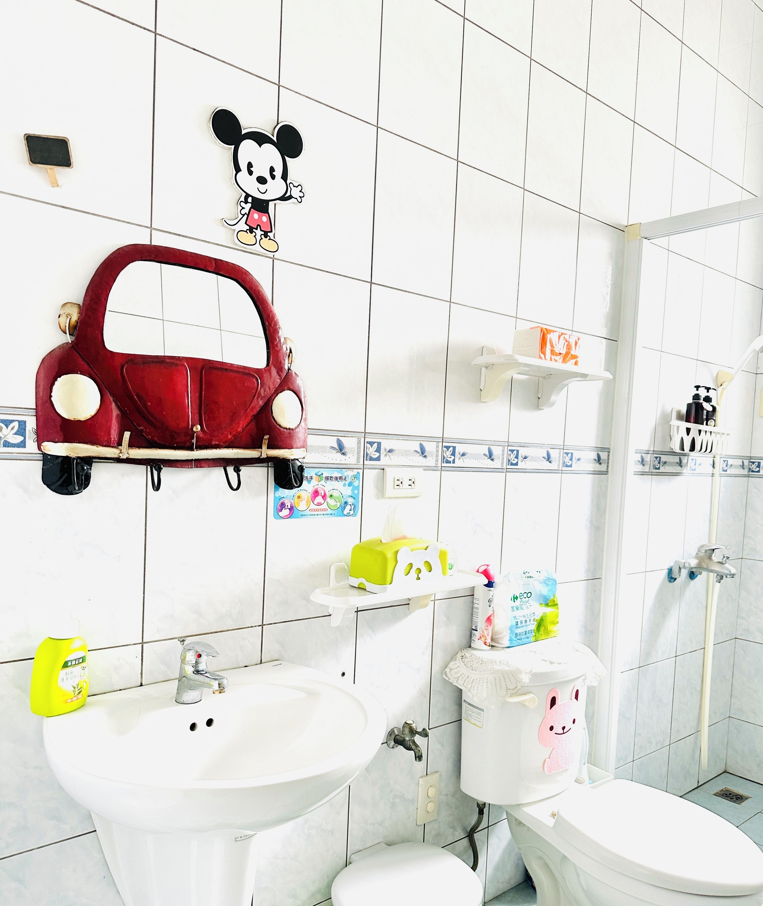 Un baño con un coche de juguete rojo, Mickey Mouse y un inodoro con diseño de conejo.