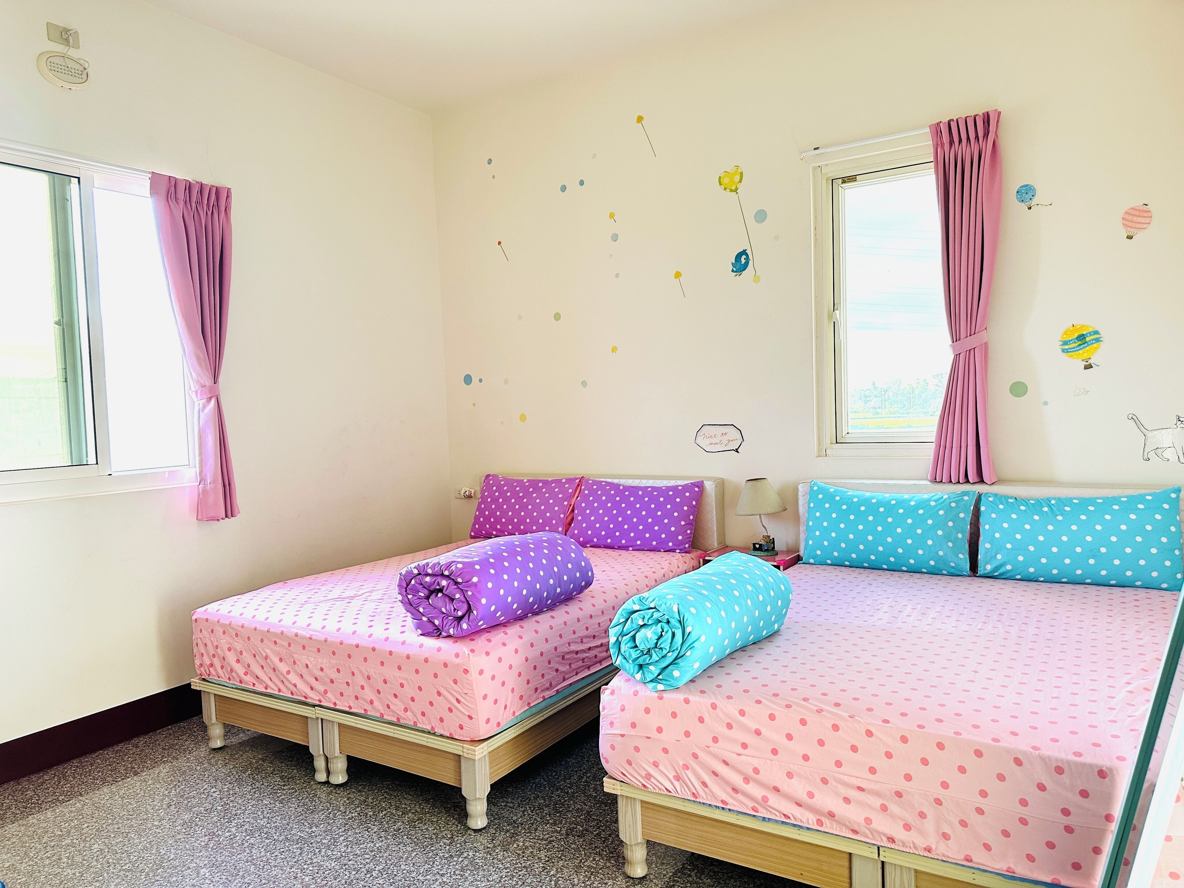Un dormitorio con dos camas individuales, cada una con una colcha de lunares, cortinas rosadas y una ventana.