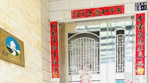L’entrée d’un hôtel, avec un banc vert, un paillasson aux motifs arc-en-ciel et des caractères chinois sur les murs.