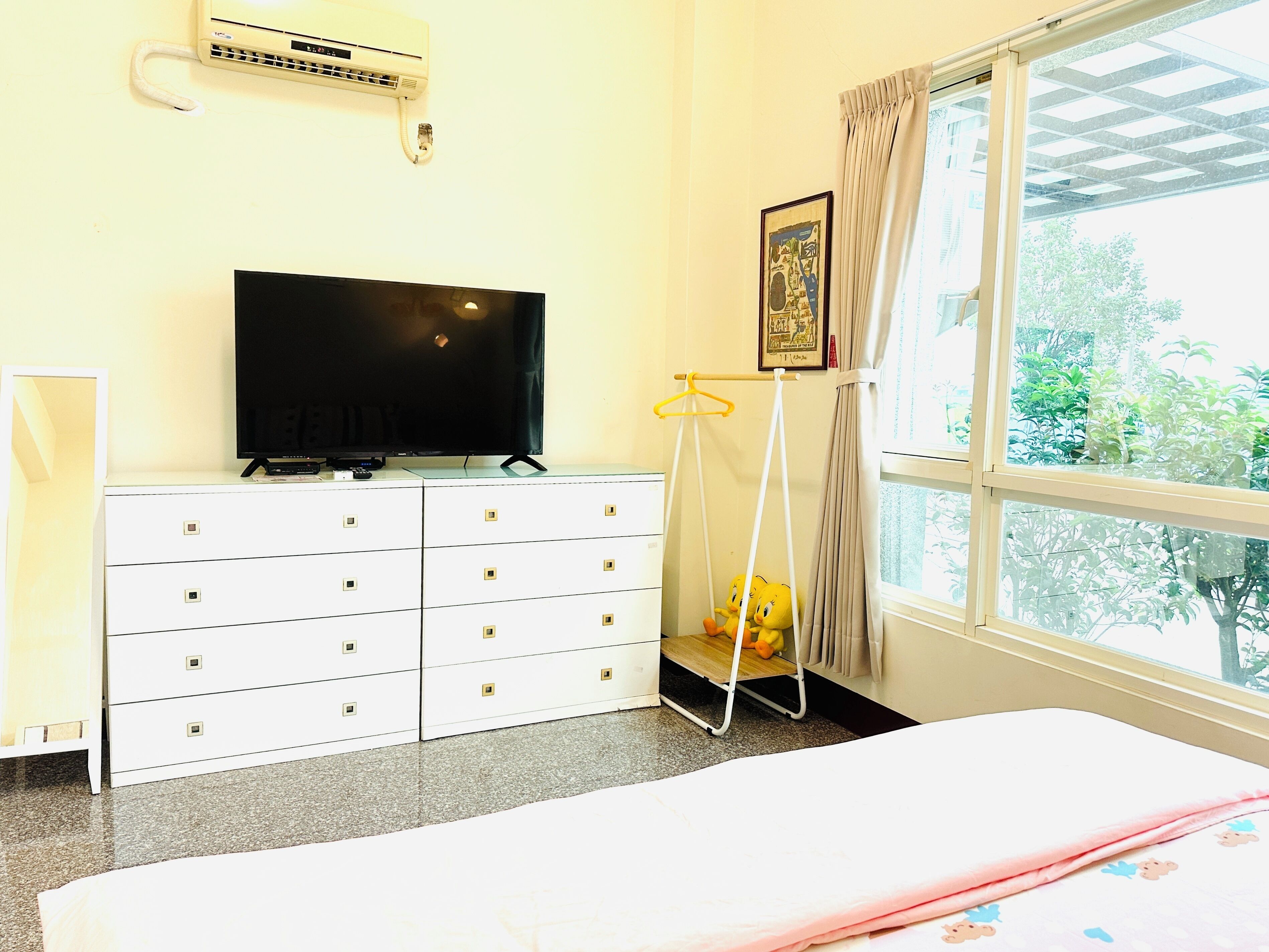 Habitación de hotel con cama, televisor en una cómoda, ventana con cortinas y un perchero.