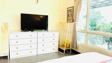 Habitación de hotel con cama, televisor en una cómoda, ventana con cortinas y un perchero.