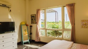 Une chambre à coucher avec un lit, un téléviseur posé sur une commode, une fenêtre avec des rideaux et une affiche accrochée au mur.