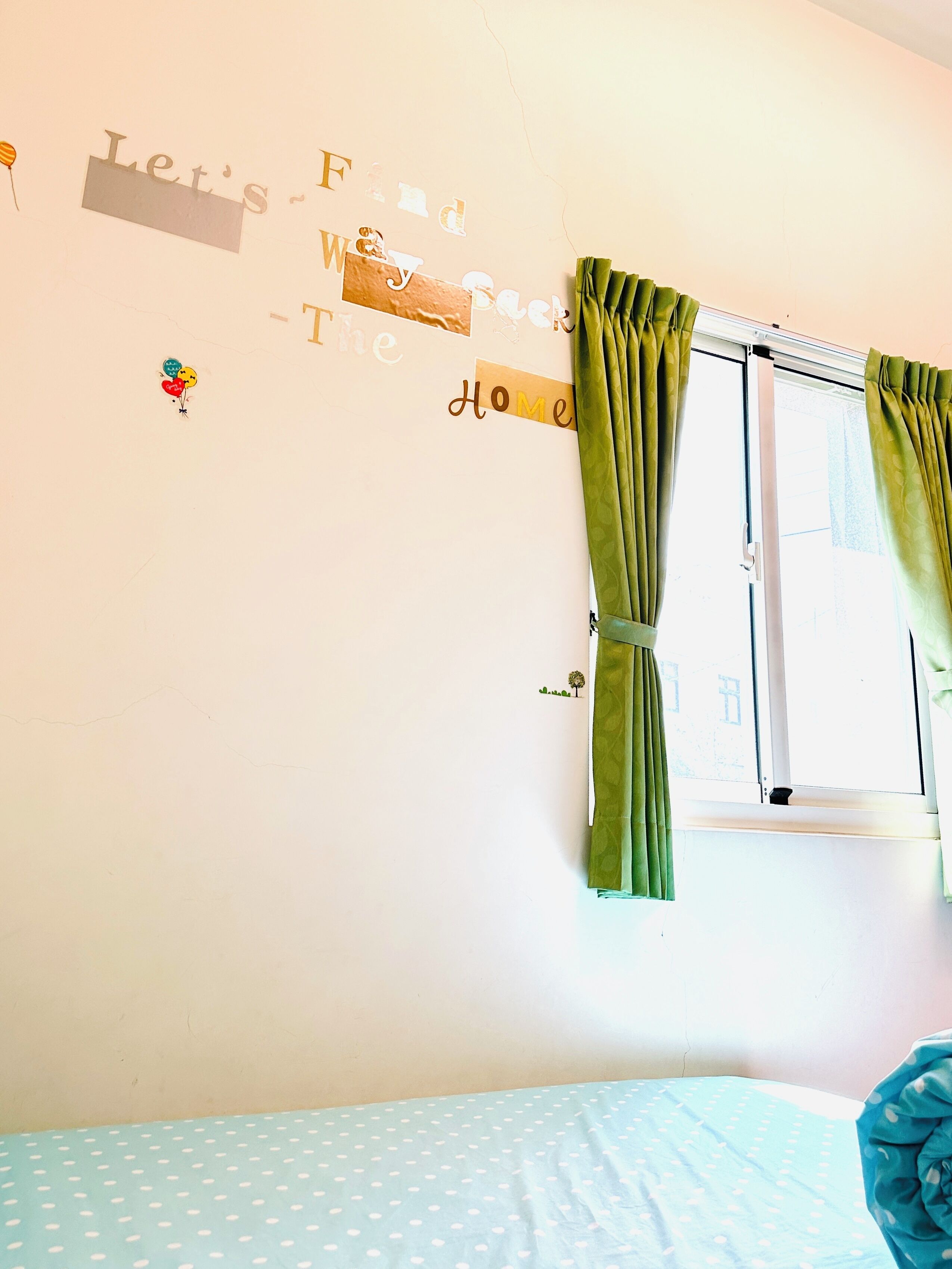 Um quarto com uma cama, uma janela com cortinas verdes e uma parede com adesivos decorativos.
