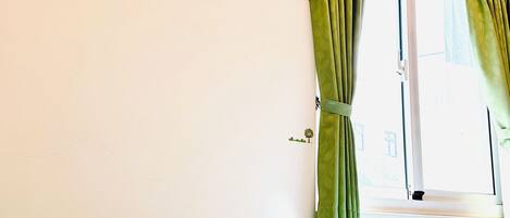Um quarto com uma cama, uma janela com cortinas verdes e uma parede com adesivos decorativos.