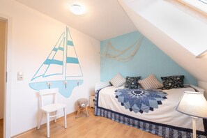 Une chambre à coucher comprenant un lit, une chaise, un petit tabouret, une décoration murale et un luminaire au plafond.