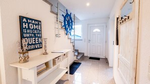A hallway with a white console table, a blue ship's wheel decoration, and a sign that reads "A MAN'S HOME IS HIS CASTLE UNTIL THE QUEEN ARRIVES." - Vacation home on the Bodden near Fischland-Darß-Zingst; fenced-in garden. Dogs Welcome (Pruchten)