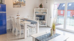 A dining area with a white table, chairs, and a blue table runner. There is a white cabinet with shelves and a small Christmas tree. - Vacation home on the Bodden near Fischland-Darß-Zingst; fenced-in garden. Dogs Welcome (Pruchten)