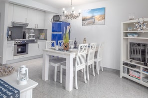 Une cuisine moderne avec des meubles blancs, un réfrigérateur bleu et un coin repas comprenant des chaises et une table, le tout dans des tons blancs.