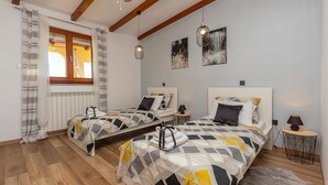 A bedroom with two beds, wooden floors, a window with curtains, and a radiator.