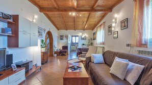 A cozy living room with a wooden ceiling, a sofa, a coffee table, and a TV. There is a kitchen area with cabinets and a dining table.