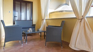 A balcony with wicker furniture, a glass table, and a door with frosted glass panels.