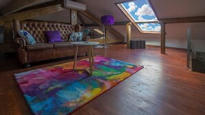 Een loftachtige kamer met een houten plafond, een bruine leren bank, een kleurrijk vloerkleed en een dakraam.