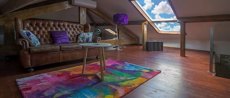 Une pièce de style loft avec un plafond en bois, un canapé en cuir marron, un tapis coloré et une lucarne.