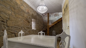Een eethoek met een witte tafel en stoelen, een kroonluchter, stenen muren en een houten plafond.