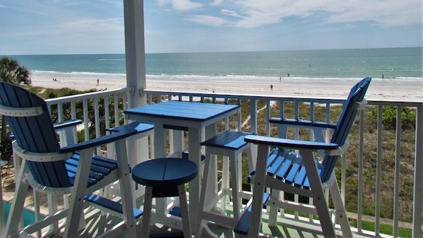 A covered outdoor seating area with a table and chairs, overlooking a beach. - Family Favorite Sea Isles- Indian Rocks Beachfront and Sunsets Galore!! (Indian Rocks Beach)