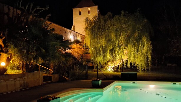 Ein Schwimmbad mit einer Fontäne, einem Turm und beleuchteten Bäumen bei Nacht.