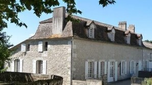 Ein Steinhaus mit steilem Dach, mehreren Schornsteinen und einem kleinen Fenster mit Rollläden.