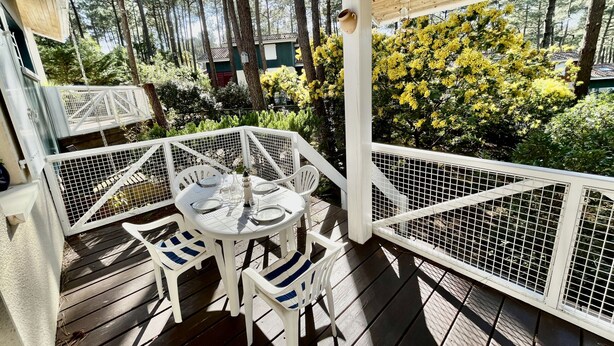 Un espace extérieur abrité, aménagé avec une table et des chaises, entouré d’une terrasse en bois et d’une rambarde blanche.