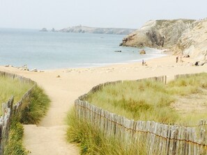 A sandy beach with a wooden fence leading to the water, rocky cliffs in the background, and a few people in the distance. - Your house loan of the sea. Beautiful decoration. (Baden)
