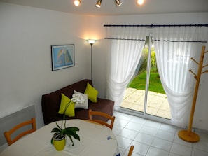 A dining area with a table, chairs, a potted plant, a sofa with cushions, a lamp, and a view of a garden through a glass door. - Your house loan of the sea. Beautiful decoration. (Baden)