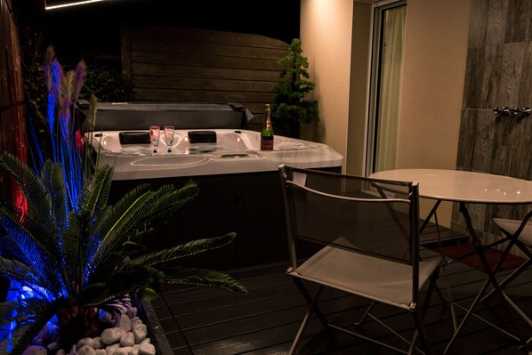 A hot tub with two glasses and a bottle, a chair, and a small tree.