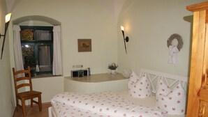 Ein Schlafzimmer mit Bett, Stuhl, kleinem Tisch, einem Fenster mit Vorhängen, einer Wandlampe und einer Wanddekoration.