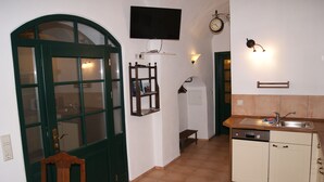 Eine Küche mit einer grünen Tür, einem Flachbildfernseher, einer Uhr und einem Spülbecken.