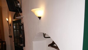 Ein schmaler Flur mit gefliestem Boden, einem an der Wand befestigten Fernseher und zwei Wandleuchten.