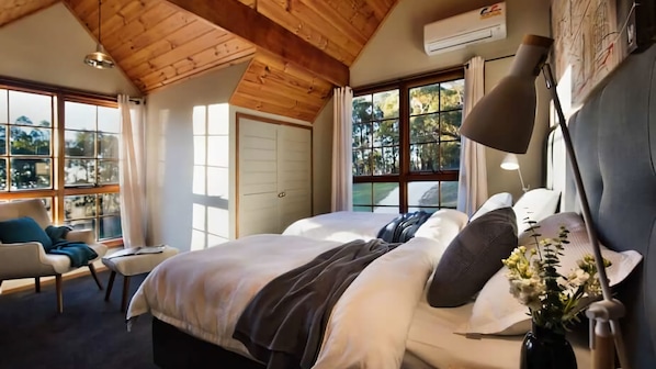 A bedroom with a large bed, a chair, a desk, and a window with a view of trees.